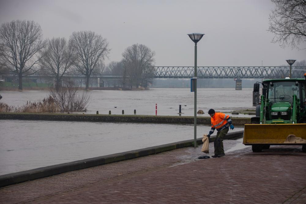 Zandzakken worden op putdeksel gelegd om te voorkomen dat ze omhoog komen door het hoge water. Foto: Mook, Hans Wildeboer